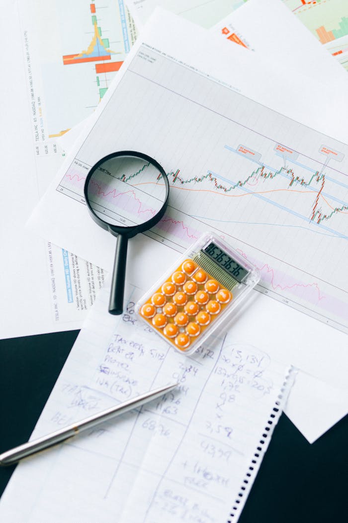 Top view of financial documents with calculator and magnifying glass, displaying charts and data analysis.